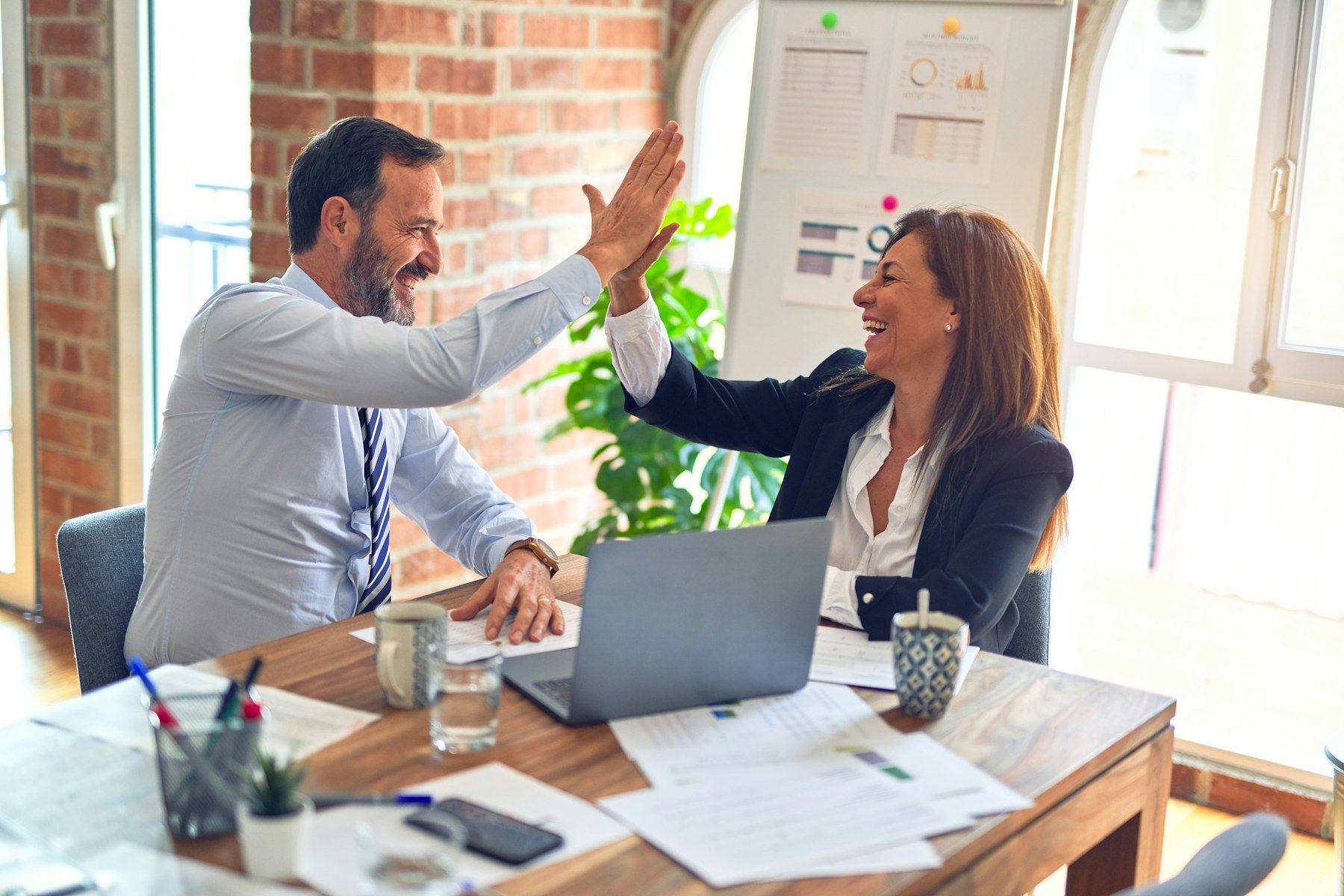 Two colleagues giving each other a high five across a desk