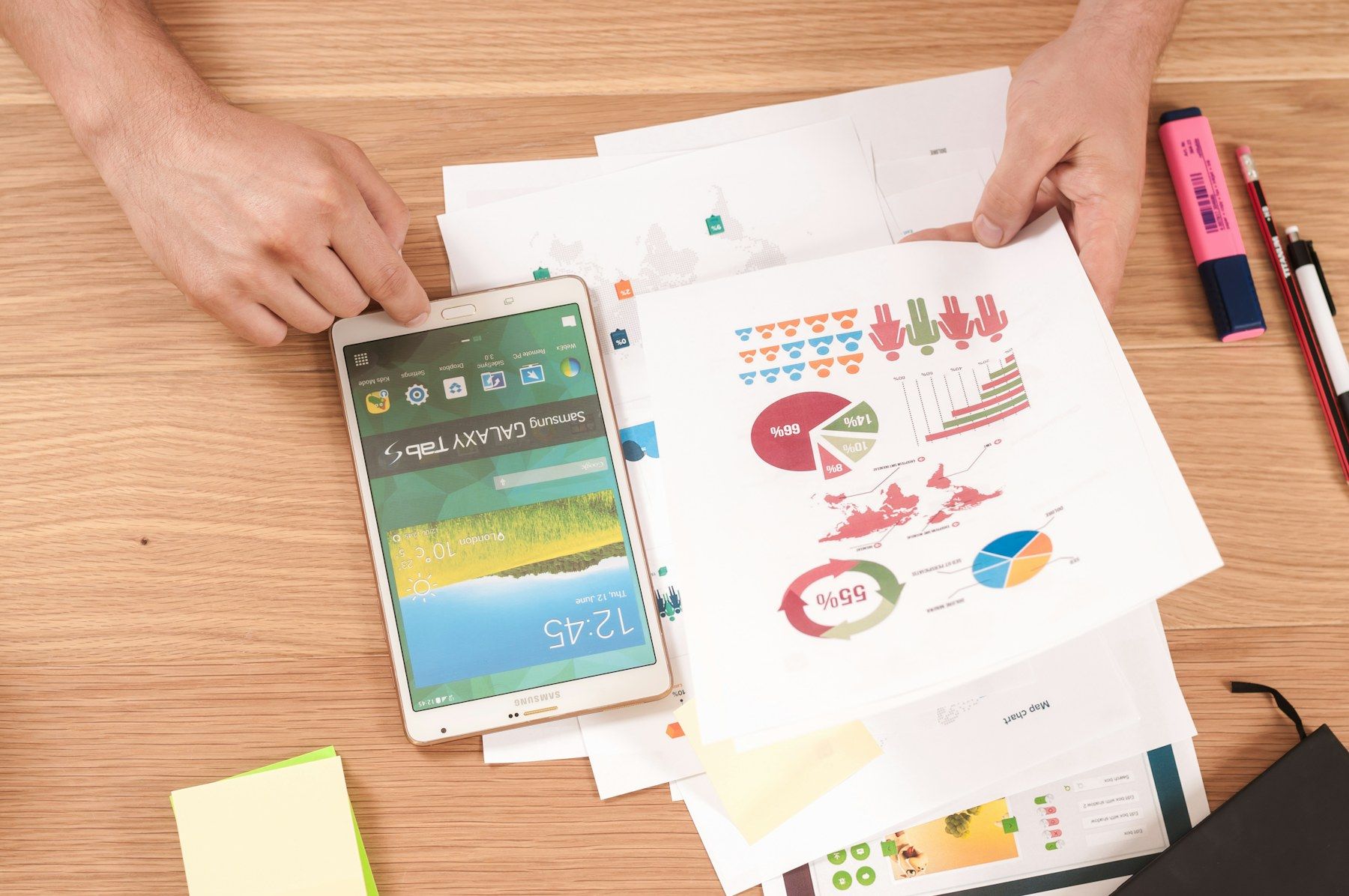 Hands reviewing printed charts and reports beside a tablet