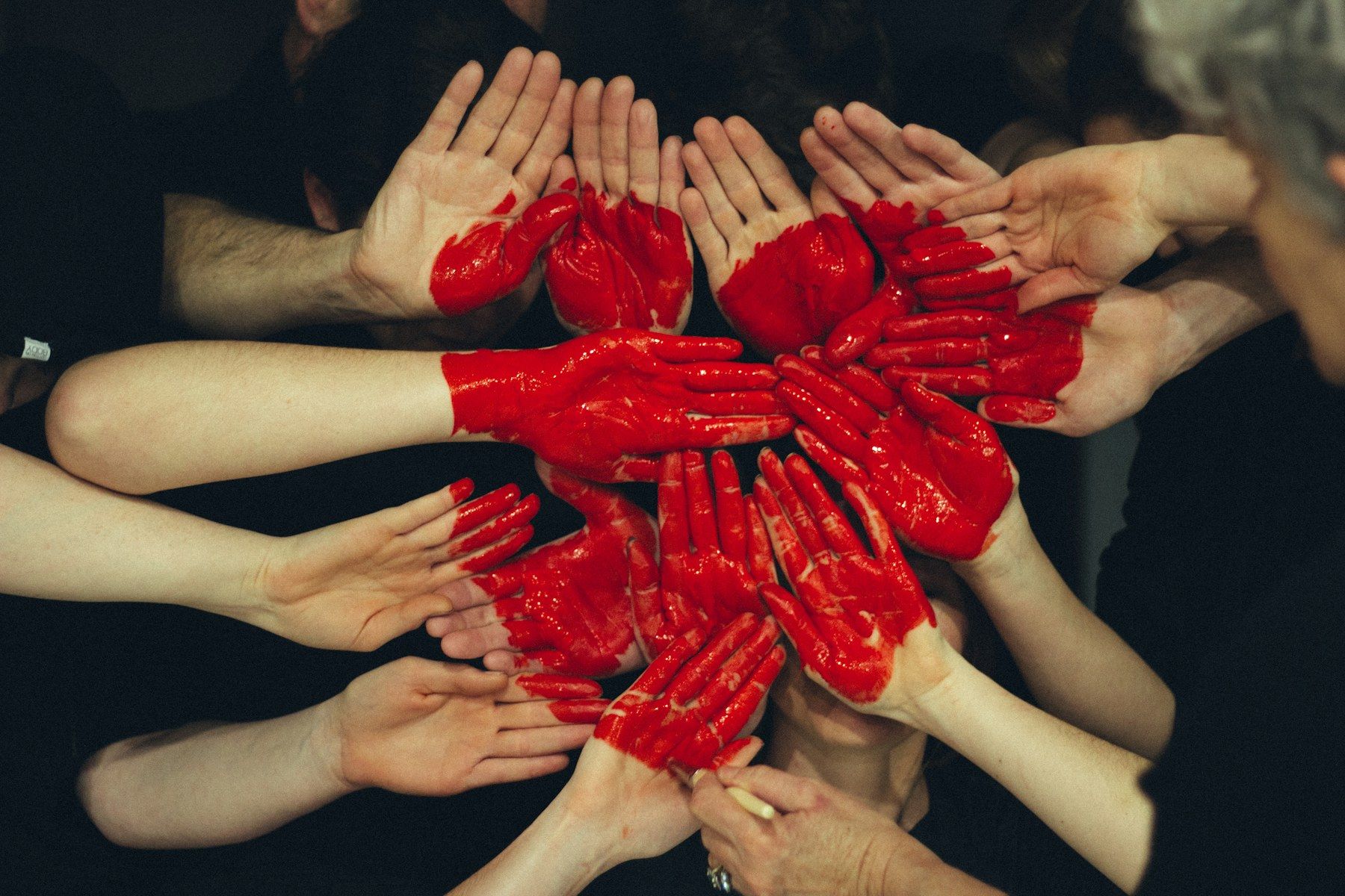 Many hands painted with red hearts held together in a circle