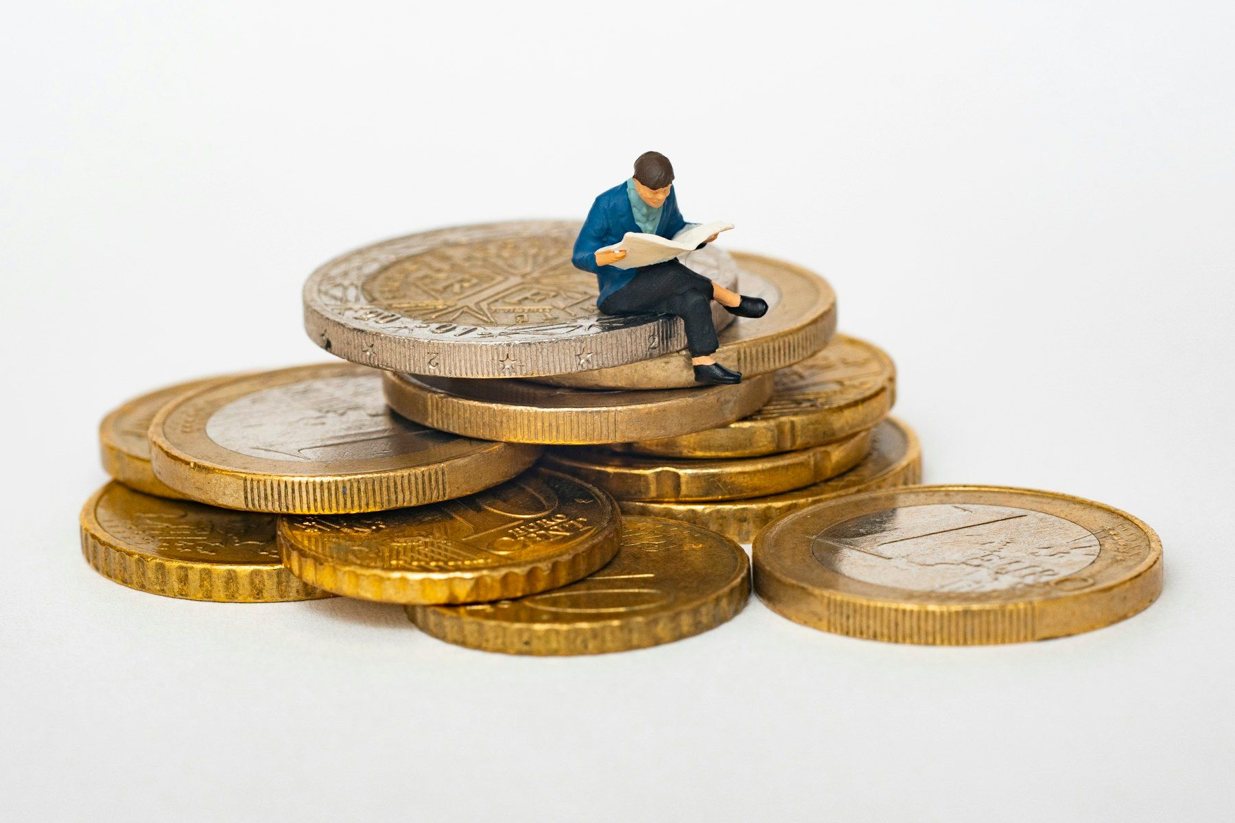 A small figure reading on top of a stack of coins