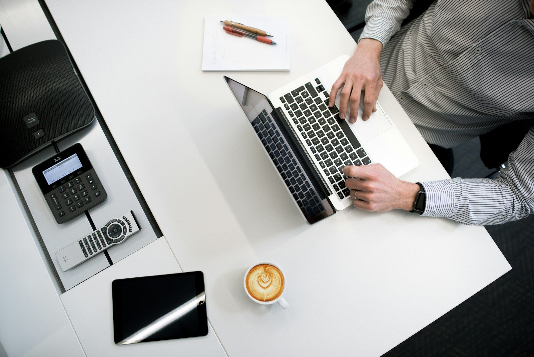 Hands working on a laptop beside a card terminal on a white desk