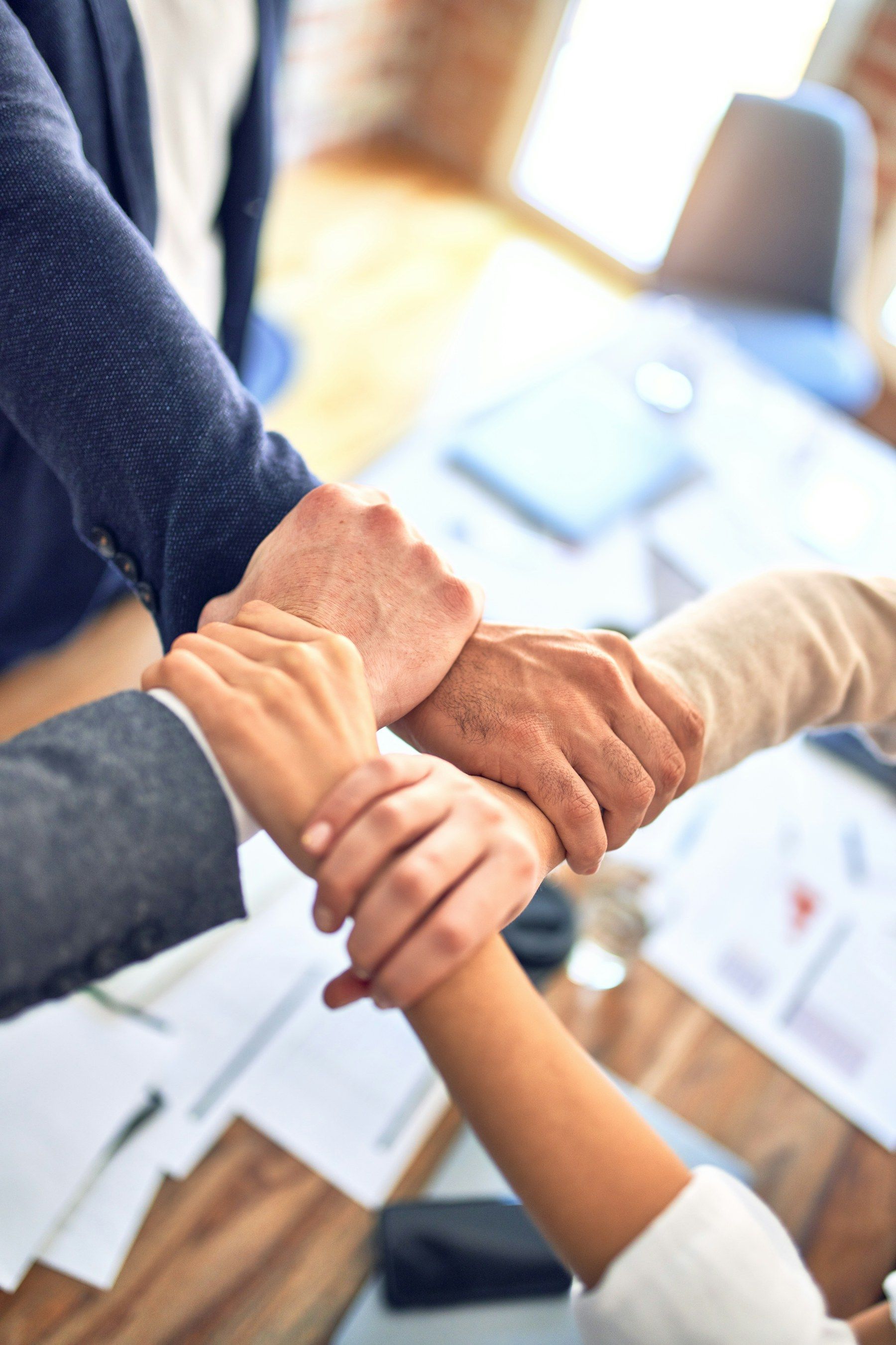 Four colleagues' hands gripping each other's wrists in a show of teamwork